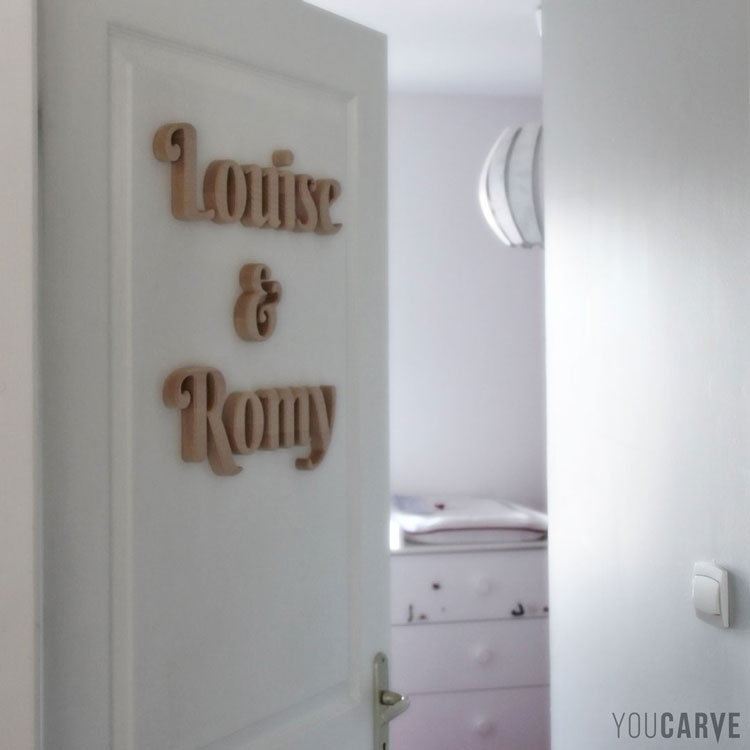Prénom en bois sur porte de chambre enfants (Louise & Romy), lettres en hêtre ép. 19 mm avec chanfreins, fixation double-face.