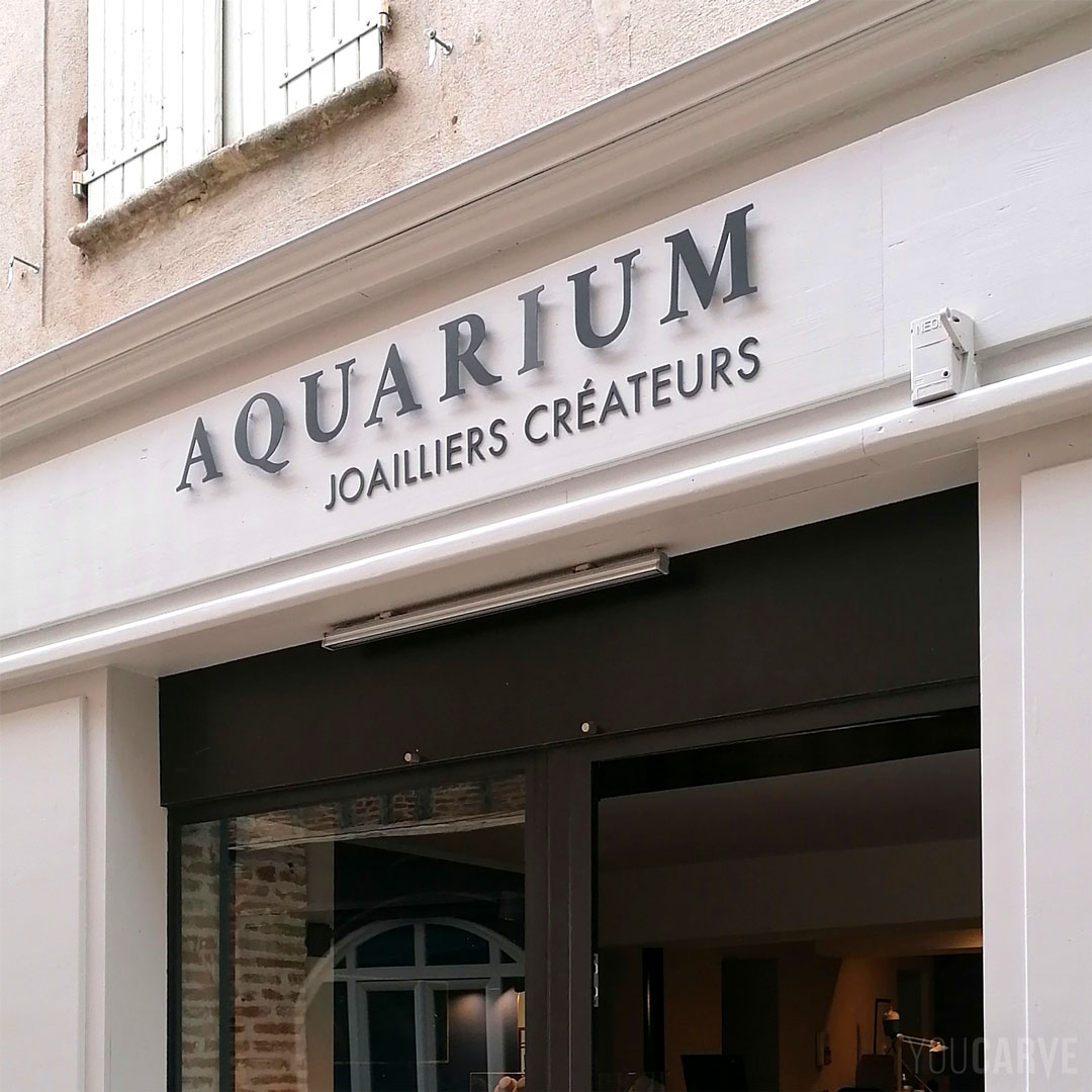 Réalisé par Aquarium : enseigne joaillerie à Lavaur, lettres découpées en aluminium-dibond gris anthracite RAL 7016 (épaisseur 3 mm), fixation sur entretoises avec gabarit de perçage.