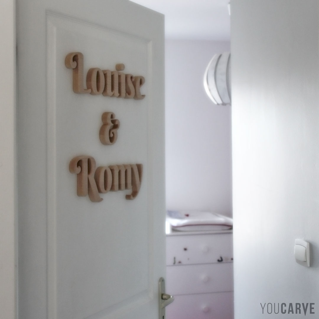 Louise & Romy, prénoms sur porte de chambre d’enfant, lettres découpées en bois (hêtre lamellé-collé épaisseur 19 mm), fixation mousse-double-face facile avec gabarit de positionnement.