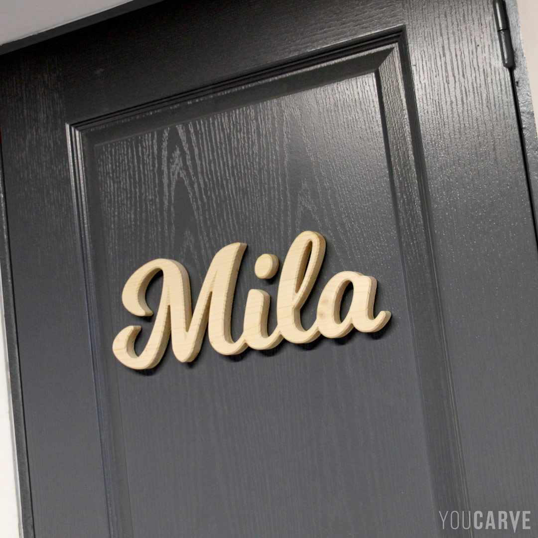 Mila, prénom en relief sur porte de chambre enfant, lettres découpées en bois (épicéa épaisseur 19 mm), fixation mousse double-face.
